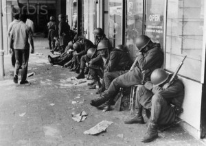 Army Guards Sleeping Against Building