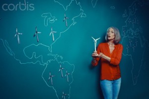Female teacher leaning against world map blowing at small wind turbine