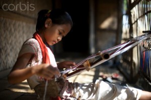 A little girl learns the skill of weaving on a handloom