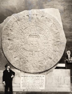 A man stands beside the calendar stone, an Aztec ancient artifact.