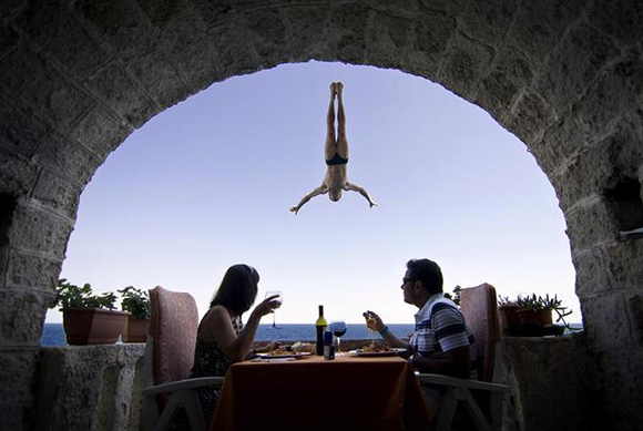 An Italian couple sits during lunch as Steve Black of Australia dives past their balcony in the lead up round four of the 2010 Red Bull Cliff Diving world series in Polignano a Mare August 5, 2010. Gary Hunt of England currently leads the six round series, with the fourth stop taking place this Sunday, August 8. REUTERS/Dean Treml/Red Bull Photofiles (ITALY - Tags: SPORT DIVING SOCIETY IMAGES OF THE DAY) FOR EDITORIAL USE ONLY. NOT FOR SALE FOR MARKETING OR ADVERTISING CAMPAIGNS