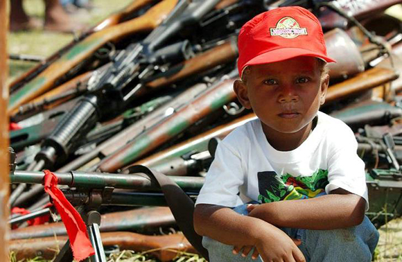 A young local boy sits in front of weapons and ammunitions that were surrendered by members of the warring Malaitan Eagle Force (MEF) in the Solomon Islands capital Honiara August 15, 2003. One of the two warring ethnic militias in the Solomon Islands staged a major ceremonial surrender of arms on Friday, handing over 90 weapons and hundreds of rounds of ammunition, saying the time for guns was over. FOR EDITORIAL USE ONLY REUTERS/Australian Army/Gary Ramage CP