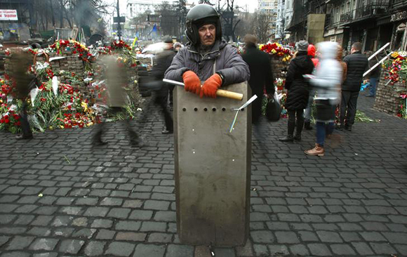 An anti-Yanukokvich protester stands behind a shield as people lay flowers at a makeshift memorial for those killed in recent violence in Kiev. Photo by David Mdzinarishvili