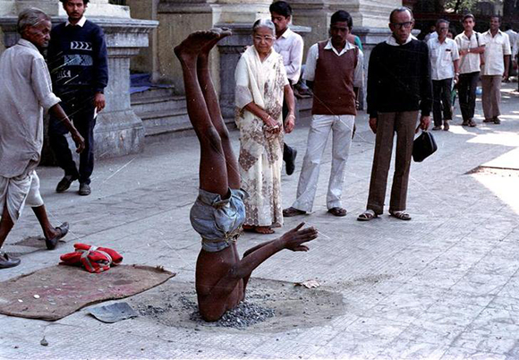 A young man, his head buried in a sidewalk hole, draws a crowd of curious onlookers in Calcutta on February 12, 1991. The man is practicing a form of yoga, Sidewalk mystics and artist like him are part of the street panorama that attracts tourists in India. REUTERS KK/IK