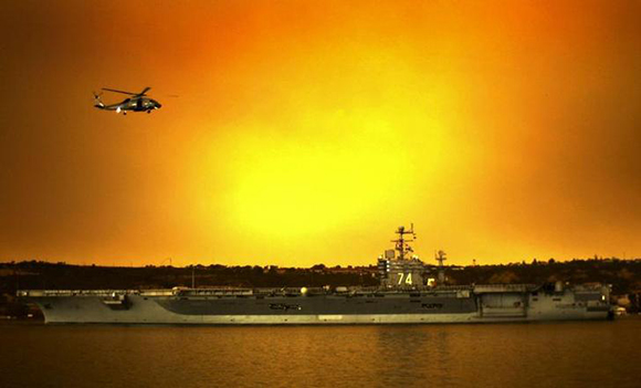 As a U.S. Navy SH-60 Seahawk flies above, the aircraft carrier USS John C. Stennis transits the San Diego channel, from Naval Air Station North Island, California, as it heads to sea under a cloud of smoke from nearby burning wildfires, October 26, 2003. Stennis is leaving port to conduct scheduled training exercises in the Southern California operating area. REUTERS/Mark Rebilas/U.S. Navy-Handout EDITORIAL USE ONLY RC/HB