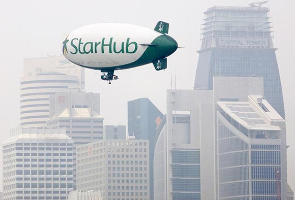 A dirigible advertising local telecommunications and cable television company StarHub flies past a haze-shrouded skyline in Singapore October 3, 2002. Singapore's pollution standards index rose to 58 on Thursday, a level indicating moderate air pollution, as fires in Indonesian Borneo and Sumatra continue to shroud parts of the region in smoke haze. REUTERS/Jonathan Drake JD