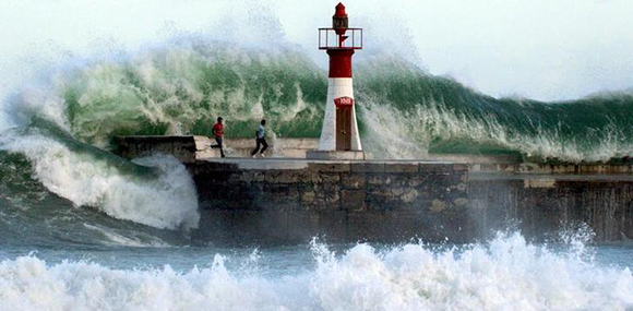 Giant waves crash over onlookers washing them off the sea wall of Cape Town's Kalk Bay harbour. Photl by Philip Massie