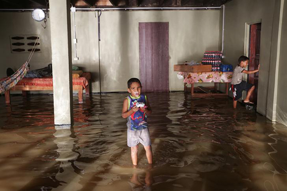 A boy eats a piece of cake as his brother wades through their flooded home in the aftermath of tropical storm Bret, in Woodland, Trinidad and Tobago June 21, 2017. REUTERS/Andrea de Silva