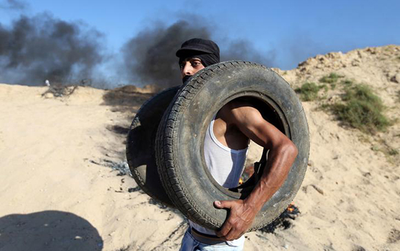 A Palestinian protester holds tyres which will be burnt during clashes near the border between Israel and Central Gaza Strip June 23, 2017. REUTERS/Ibraheem Abu Mustafa