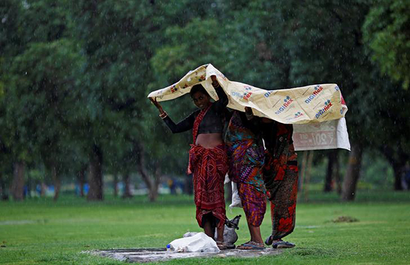 Women use a plastic sheet to cover themselves from rain at the India Gate lawns in New Delhi, India, June 28, 2017. REUTERS/Adnan Abidi