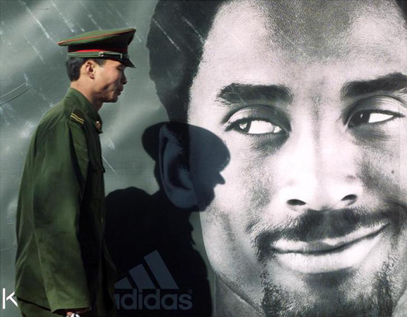 A People's Libration Army (PLA) soldier walks past an advertisement board for a German sports equipment manufacturer featuring American NBA star, Kobe Bryant, in Beijing November 17, 2000. Foreign companies are increasing their promotion and advertisement budget in a race to capture a large market share when China eventually join the World Trade Organisation (WTO).