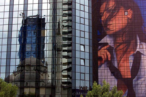 A mosque silhouette is reflected on the mirror glass covered facade of a skyscrape housing banking companies and holdings next to a giant bilboard advertising a clothing company in the financial district in Istanbul June 22, 2001. Turkey's financial markets are nervously awaiting a verdict on Friday by the Constitutional Court on whether to ban the main opposition party for Islamic subversion, which may trigger polls at a time of financial crisis.