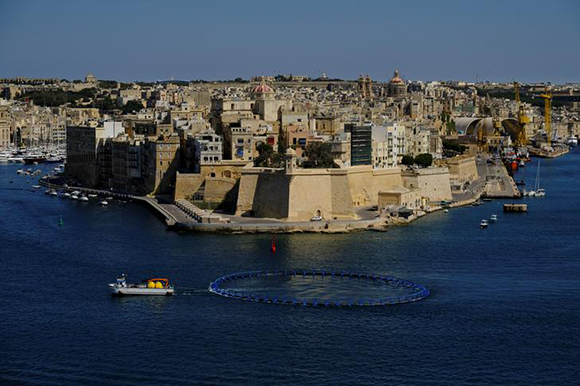A fishing boat towing a tuna pen passes the medieval fortified town of Senglea on its way out of Valletta's Grand Harbour, Malta. Photo by Darrin Zammit Lupi