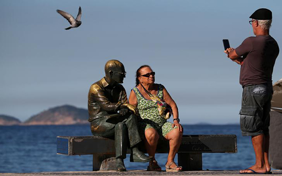 An elderly woman poses for picture next to a statue of Brazilian writer Carlos Drummond de Andrade on Copacabana beach in Rio de Janeiro, Brazil. Photo by Sergio Moraes