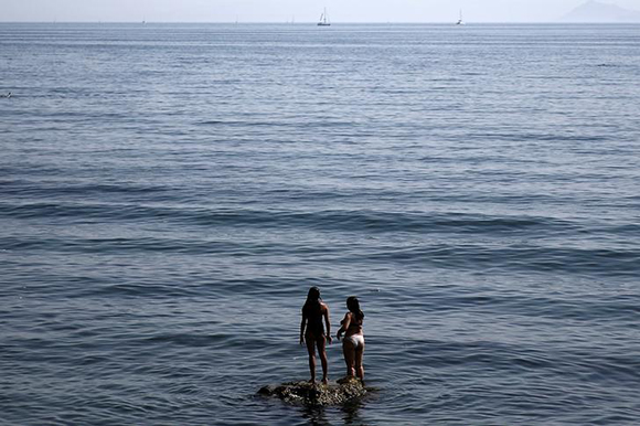 Two girls stand on a rock at a beach in Alimos suburb, south of Athens, Greece. Photo by Costas Baltas