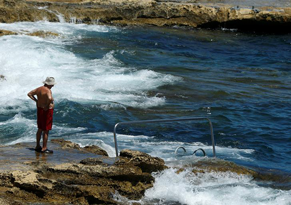 An elderly man stands on a rocky beach looking at the sea in Sliema, Malta. Photo by Darrin Zammit Lupi