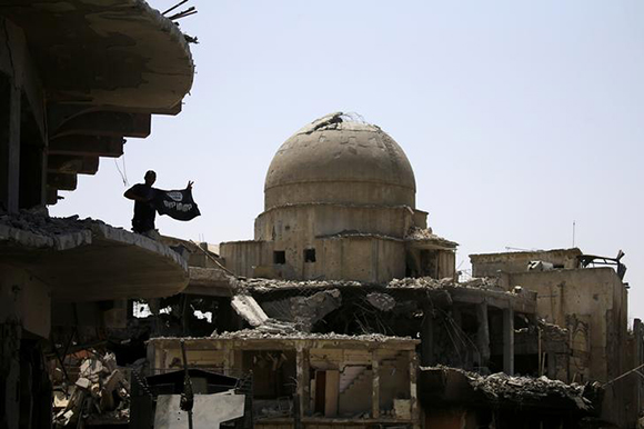 A member of Iraqi security forces holds a flag of Islamic State militants on the top of a destroyed building from clashes in the Old City of Mosul, Iraq July 10, 2017. Photo by Thaier Al-Sudani