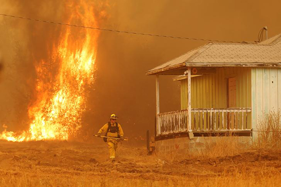  A firefighter walks near a home as flames from the fast-moving Detwiler fire approach in Mariposa, California U.S. July 19, 2017. Photo by Stephen Lam