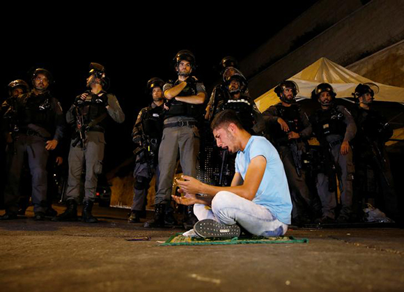  Israeli border police stand guard as a Palestinian man takes part in evening prayers outside the Lion's Gate of Jerusalem's Old City July 23, 2017. Photo by Ammar Awad