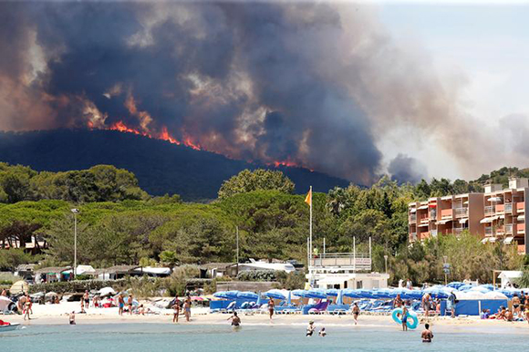  Flames and smoke fill the sky above a burning hillside as tourists swim on the beach in Bormes-les-Mimosas, in the Var department, France, July 26, 2017. Photo by Jean-Paul Pelissier