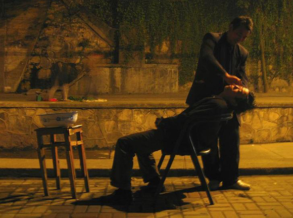  A street-barber shaves a customer under a bridge late at night in Beijing. Photo by David Gray