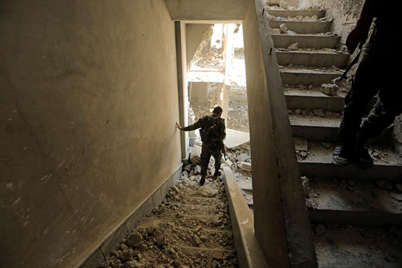 A member of the Syrian Democratic Forces walks down the stairs of a damaged building during fights with Islamic State fighters in Hisham Bin Abdelmalik, a district of Raqqa, Syria August 13, 2017. Photo by Zohra Bensemra