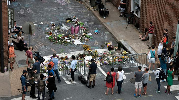 Mourners and passersby surround an impromptu memorial of flowers and chalk notes written on the street commemorating the victims at the scene of the car attack on a group of counter-protesters during the "Unite the Right" rally in Charlottesville, Virginia, August 14, 2017. Photo by Justin Ide