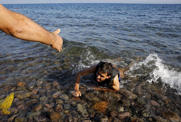A local man helps a Syrian refugee who jumped off board from a dinghy as he swims exhausted at a beach on the Greek island of Lesbos. Photo by Yannis Behrakis