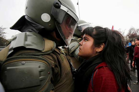 A demonstrator looks at a riot policeman during a protest marking the country's 1973 military coup in Santiago, Chile. Photo by Carlos Vera