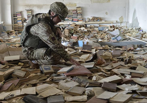 A Ukrainian serviceman looks through a book at an abandoned library near his position on the front line in the town of Maryinka, Ukraine. Photo by Oleksandr Klymenko