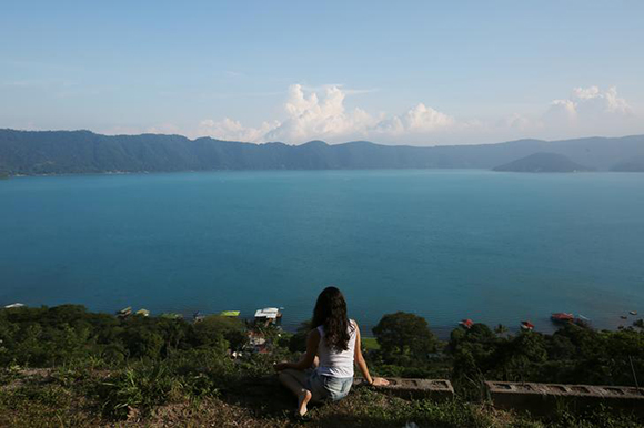 A woman poses for a picture with the Coatepeque Lake as background in the town of El Congo, El Salvador Photo by Jose Cabezas