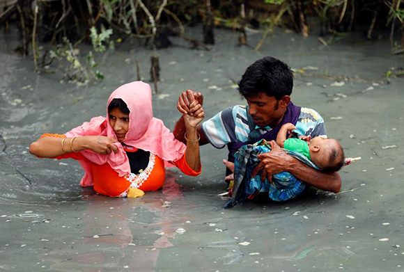 Rohingya refugees carry their child as they walk through water after crossing border by boat through the Naf River in Teknaf, Bangladesh, September 7, 2017. Photo by Mohammad Ponir Hossain