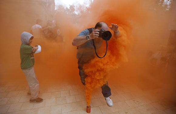A photographer jumps over a smoke canister during a demonstration by firefighters, security and military personnel against cuts in their salaries imposed by Spanish Government, in the Andalusian capital of Seville. Photo by Marcelo del Pozo 
