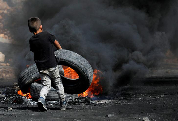  A Palestinian boy puts a tyre on fire during clashes with Israeli troops near the Jewish settlement of Qadomem, in the West Bank village of Kofr Qadom, near Nablus, October 20, 2017. Photo by Mohamad Torokman 