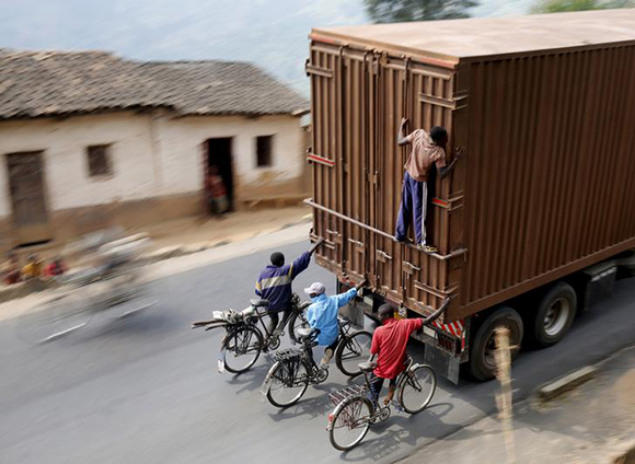  Cyclists hang on to the back of a truck outside the capital Bujumbura. Photo by Mike Hutchings 
