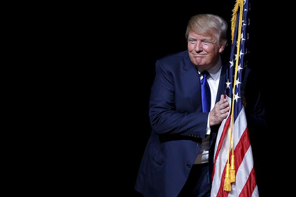 U.S. Republican presidential candidate Donald Trump hugs a U.S. flag as he takes the stage for a campaign town hall meeting in Derry, New Hampshire. Photo by Brian Snyder 