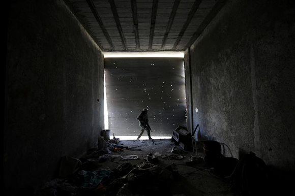  A Free Syrian Army fighter walks as he holds his weapon in a damaged shop, in the town of Tadef, Aleppo Governorate, Syria. Photo by Khalil Ashawi 