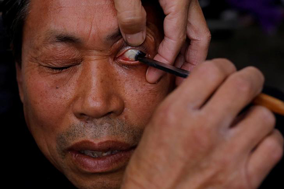  A customer looks on as Xiong Gaowu, a 62-year old street barber cleans his eye using the straight razor in Chengdu, Sichuan province, China. Photo by Tyrone Siu 