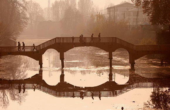  People walk on a wooden footbridge across a canal during an autumn day in Srinagar. Photo by Danish Ismail 