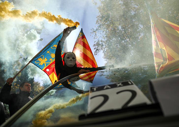  A masked protestor holds a smoke bomb during a strike by taxi drivers to protest what they say is unfair competition from new car sharing companies such as Uber and Cabify, in Madrid , Spain, November 29, 2017. Photo by Juan Medina 