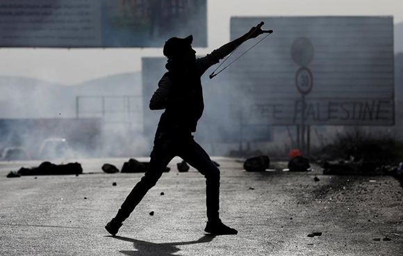  A masked Palestinian demonstrator uses a slingshot to hurl stones towards Israeli troops during clashes at a protest against U.S. President Donald Trump's decision to recognise Jerusalem as the capital of Israel, near the West Bank city of Nablus, December 29, 2017. Photo by Mohamad Torokman 