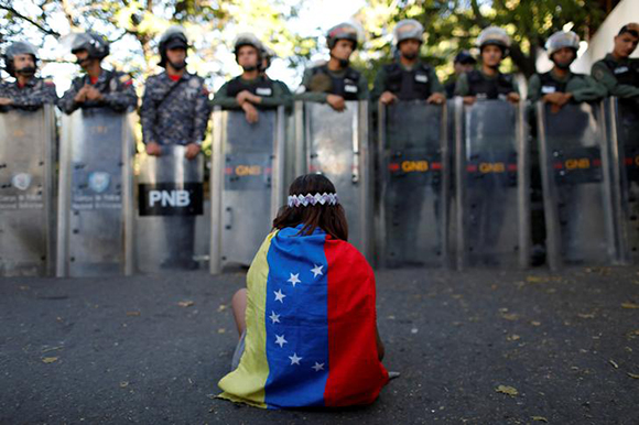  A girl wears a Venezuelan flag as Venezuelan security forces block access to opposition supporters and mourners of rogue ex-policeman Oscar Perez to the main morgue of the city, in Caracas, Venezuela January 20, 2018. Photo by Marco Bello 