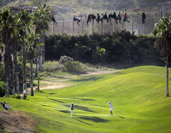 A golfer hits a tee shot as African migrants sit atop a border fence during an attempt to cross into Spanish territories between Morocco and Spain's north African enclave of Melilla Photo by Jose Palazon 